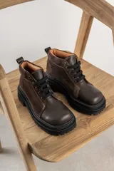 Borcegos de punta cuadrada con diseño acordonado, combinando paneles de cuero texturizado y gamuza en tonos marrones. Presentan una suela track gruesa de goma negra y cordones negros.