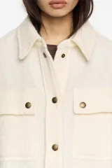 Sobrecamisa de corte oversize confeccionada en mezcla de lana, con cuello camisero, cierre frontal de botones y mangas largas con puños abullonados. Presenta bolsillos frontales con tapeta en el pecho y bolsillos laterales en el bajo, además de un detalle de pliegue en el canesú de la espalda.