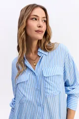 Camisa de manga larga con estampado de rayas verticales en tonos azul y blanco. Presenta cuello clásico, cierre frontal con botones y dos bolsillos tipo cargo en el pecho. Su diseño es de corte relajado y holgado.