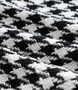 Blazer de sastrería confeccionado en tejido tweed con estampado pied de poule en blanco y negro. Presenta cuello con solapa, cierre frontal con un botón, mangas largas y bolsillos frontales con solapa.