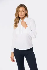 Camisa blanca de manga larga con cuello y tapeta de medio botón. Presenta dos bolsillos frontales con tapa y botones metálicos. Las mangas tienen presillas para sujetar el puño enrollado.