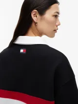 Chomba de rugby de manga larga Tommy Hilfiger en colaboración con Cadillac Formula 1 Team. Presenta un diseño en bloques de color negro, blanco y rojo, con cuello estilo rugby en color blanco y cierre frontal oculto. Incluye el logo de Cadillac en fuente script y el logo de Tommy Hilfiger estampados en el pecho.