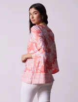 Blusa color salmón con estampado floral blanco, cuello redondo con abertura y mangas 3/4 acampanadas.