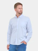 Camisa de corte clásico confeccionada en tela Oxford con diseño de rayas verticales finas en tono celeste claro sobre fondo blanco. Presenta cuello abotonado, cierre frontal con botones y un bolsillo aplicado en el pecho.