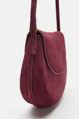 Bolso bandolera de piel de ante color bordó, con solapa curva, cierre de clip metálico y correa larga ajustable.