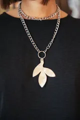 Collar de cadena de eslabones plateados con dije colgante de alpaca en forma de hoja con textura irregular. El diseño permite múltiples formas de uso.
