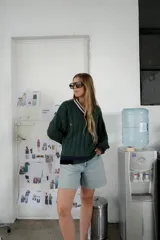 Buzo tejido de punto con escote en V, manga larga y diseño holgado. Presenta un patrón de rayas verticales en relieve y detalles de franjas en contraste en el cuello, puños y ruedo. Incluye un pequeño bordado en el pecho.