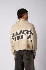 Campera tejida de punto con cierre frontal completo, cuello tipo polo y diseño con franja horizontal en contraste con estampado gráfico. Presenta puños y ruedo acanalados, con corte holgado.