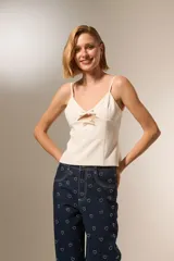 Musculosa de color blanco con breteles finos, escote en V y detalle de aberturas frontales con lazos decorativos.