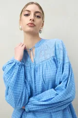 Blusa holgada color celeste con estampado de cuadrillé, mangas largas abullonadas y escote con lazo. Presenta un canesú superior de encaje floral en el mismo tono.