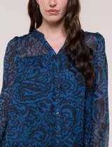 Blusa de silueta holgada y caída fluida, confeccionada en gasa liviana con estampado paisley en tonos azules y negros. Presenta cuello mao con escote en V, cartera frontal con botones, canesú con frunces y mangas largas con puños elastizados.