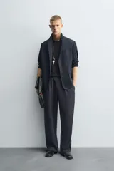 Pantalón negro de corte relajado con cintura elástica ajustable y pliegues en la parte delantera. Presenta bolsillos laterales y bolsillos traseros de parche.