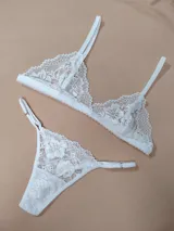 Conjunto de lencería de dos piezas confeccionado en encaje blanco con diseño floral. Incluye un soutien tipo triángulo con tirantes regulables y una bombacha tipo colaless con tiras laterales ajustables.