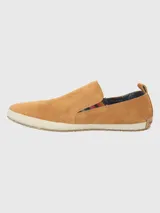 Alpargata Hush Puppies de gamuza color mostaza, con suela de yute trenzado y base de goma. Presenta un detalle elástico lateral con diseño multicolor y forro interior de algodón orgánico.
