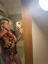 Minivestido con estampado de mariposas en tonos naranja y negro. Diseño ajustado con escote halter asimétrico y abertura en la cintura.