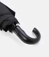 Paraguas plegable de color negro, con estructura metálica y mango curvo de plástico negro.