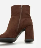 Bota de caña corta con acabado aterciopelado, punta cuadrada y taco bloque alto. Presenta un diseño minimalista y estructurado con cierre lateral.