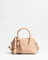 Cartera chica tipo handbag de color beige, con textura granulada, doble asa superior, correa ajustable y desmontable, herrajes metálicos dorados y detalle de llavero colgante con forma de borla. Cuenta con cierre superior y logo de la marca estampado en el frente.