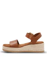 Sandalias Hush Puppies modelo Lili, color marrón, con plataforma de yute y suela de caucho. Presentan una tira ancha en el empeine y una correa ajustable al tobillo con hebilla metálica dorada.