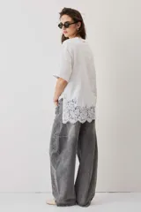 Remera blanca de algodón, de corte oversize, manga corta y cuello redondo, con detalle de aplique de encaje floral en el borde inferior.