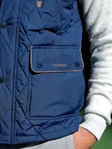 Chaleco acolchado de color azul oscuro con diseño de rombos, cuello alto, cierre frontal con botones a presión y bolsillos delanteros con solapa y detalles en contraste.