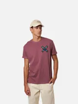 Remera Blue Banana de algodón orgánico color gris oscuro, con manga corta y corte clásico. En la espalda presenta una gran estampa en forma de 'X' con patrón multicolor de estilo étnico y el logo de la marca en la parte superior.