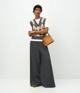 Pantalón de corte amplio tipo pantalona, confeccionado en tejido con patrón de rayas diplomáticas. Presenta cintura alta con trabillas para cinturón y cierre frontal tradicional.