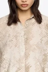 Camisa de corte boxy con cuello camisero, cierre frontal de botones y mangas largas con puños abotonados. Presenta un estampado animal print en tonos neutros.