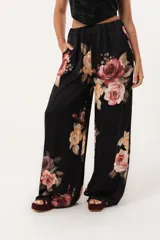 Pantalón palazzo negro con estampado floral en tonos rosa, naranja y amarillo. Tiene cintura alta con elástico.