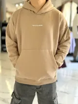 Canguro oversize tostado con capucha y bolsillo tipo canguro, confeccionado con diseño holgado. En la espalda presenta un estampado en color blanco con las palabras "FOCUS FUTURE", gráficos de estrellas y un diseño de globo terráqueo acompañado del texto "EST. 2021".