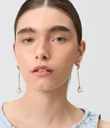 Aros colgantes dorados de diseño alargado con dije de perla en el extremo.