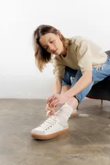 Zapatillas color marfil con detalles dorados en el talón y ojales metálicos. Suela de goma caramelo y cordones beige.