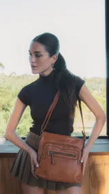 Bandolera de símil cuero color negro con dos bolsillos frontales con cierre, un bolsillo trasero y tres bolsillos internos. Detalles de tachas metálicas y correa larga regulable.