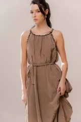 Vestido largo color marrón, con escote redondo y tirantes decorados con perlas. Presenta un lazo para ajustar la cintura y una falda con movimiento.