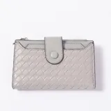 Billetera de cuero sintético color gris con diseño trenzado y cierre de solapa con botón a presión. Cuenta con compartimento con cierre superior y tarjetero frontal.