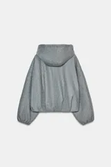 Chaqueta estilo bomber de corte oversize en color marrón oscuro, confeccionada en tejido suave. Presenta capucha con cordones ajustables, cierre frontal con cremallera, mangas largas con puños elásticos y bolsillos delanteros de vivo. El bajo cuenta con detalle de pliegues.