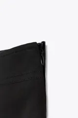 Falda pantalón negra de tiro medio, confeccionada en algodón, con pliegue frontal y maxi bolsillos cargo con solapa y cremallera en ambos lados.