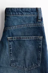 Jean de tiro alto y diseño barrel en denim de algodón azul, con corte de cinco bolsillos, cierre frontal con botón y cremallera, y piernas de corte curvo y holgado.