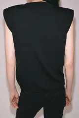 Top de punto negro con cuello redondo, manga sisa, hombreras y detalle de pliegues en la parte delantera.