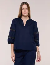 Blusa de calce suelto y caída ligera, color azul marino. Presenta escote en V con cuello Mao pequeño, mangas tres cuartos abullonadas con elástico en los puños y detalles de calado o puntilla encastrada.