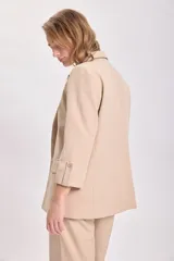 Blazer de color visón con mangas tres cuartos, solapas clásicas y cierre frontal con un botón. Presenta bolsillos laterales con solapa.