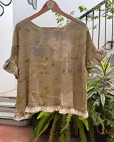 Top de lino con diseño de impresión botánica (ecoprint) en tonos verdes y tierra. Presenta un corte holgado, mangas cortas con volados y un volado decorativo en el ruedo.