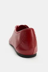 Zapato plano de piel color rojo, con cierre de cordones al tono, puntera redonda y suela baja.
