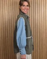 Chaleco de denim color marrón, confeccionado en 100% algodón, con bolsillos frontales amplios, cierre de botones y costuras decorativas bordadas en blanco en los bordes y los bolsillos.
