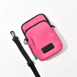 Porta celular fucsia con correa negra ajustable. Tiene dos compartimentos con cierre y un aplique rectangular negro en el frente.