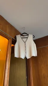 Chaleco tejido de punto color beige con corte sastrero, abotonadura frontal y detalle de bordado a mano en contraste a lo largo de los bordes.