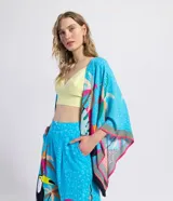 Kimono abierto de manga corta amplia, confeccionado en viscosa con estampado tropical de tucanes y palmeras sobre fondo celeste, con detalles en rosa, amarillo y negro, y terminación de flecos en los bordes.