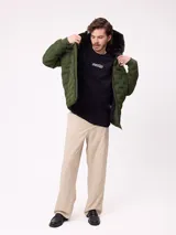 Campera puffer con capucha, color verde militar, con cierre frontal y bolsillos laterales. Presenta un diseño acolchado con costuras termoselladas y puños elásticos.