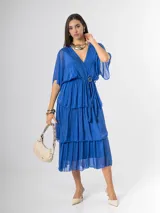 Vestido midi de seda italiana color azul, con escote en V, mangas murciélago amplias, falda de tres volados y cintura elastizada con lazo ajustable al tono y hebilla circular dorada.