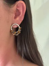 Aro de plata con forma de herradura, decorado con cuentas de vidrio facetadas en tonos ámbar y marrón, sujetas con alambre fino.